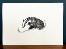 Load image into Gallery viewer, Badger giclée print in black frame on wooden surface. Navy blue wall behind.