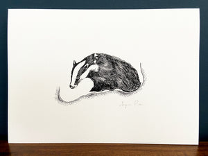 Badger giclée print in black frame on wooden surface. Navy blue wall behind.