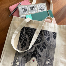Load image into Gallery viewer, Red Riding Hood illustration canvas tote bag on a wooden background with pen, books and purse spilling out.
