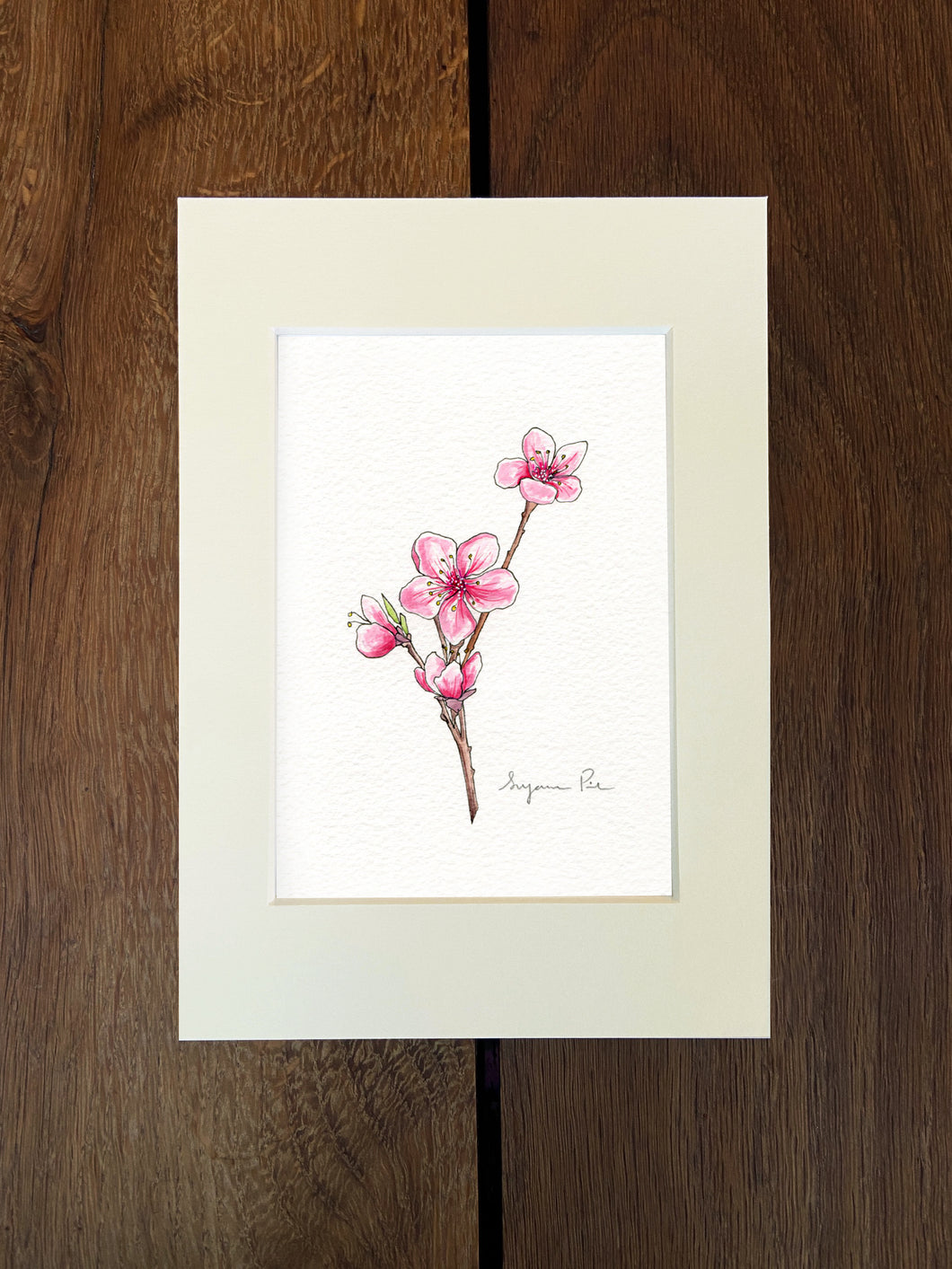 Handpainted cherry blossom design using fineliner, watercolour and white ink in an ivory mount on a wooden background.