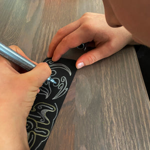 Child drawing a pattern design on a bookmark using a silver marker pen.