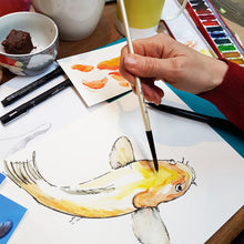Load image into Gallery viewer, Person painting a fish with watercolors on a table with art supplies.
