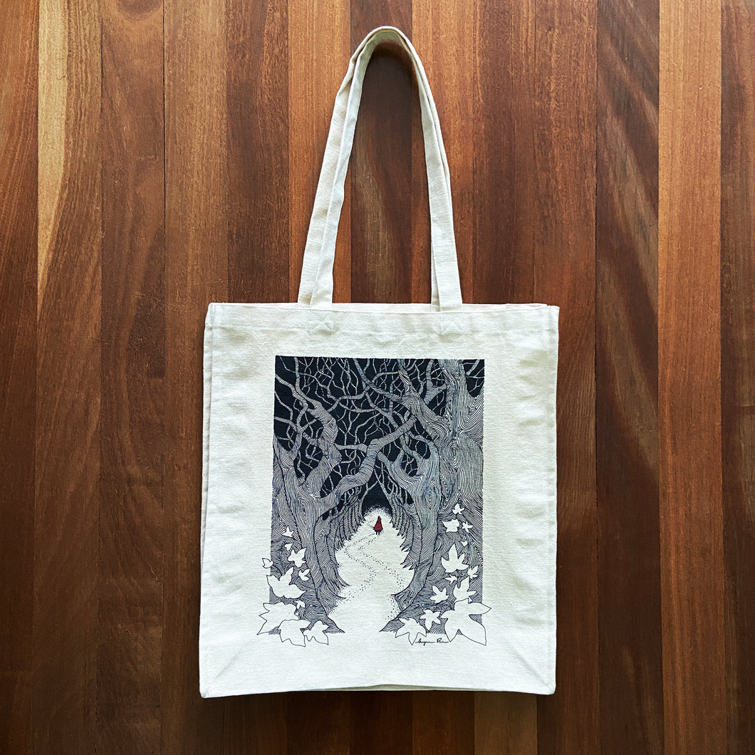 Canvas tote bag lying flat on a wooden background with a Red Riding Hood illustration design.