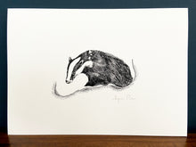 Load image into Gallery viewer, Badger giclée print in black frame on wooden surface. Navy blue wall behind.
