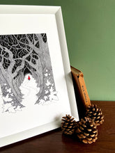 Load image into Gallery viewer, Red Riding Hood giclée print with handpainted watercolour detail in red. Print is in white frame, standing on wooden surface with green wall behind. Pine cones anad book of wild animals stands beside.
