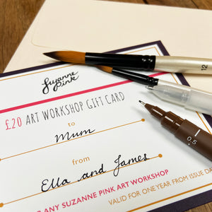 Art workshop gift card back with pens and paintbrushes and envelope on a wooden table