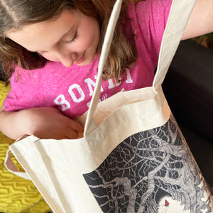 Girl with a pink t-shirt on looking inside a canvas tote bag and smiling.