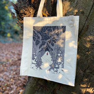 Canvas tote bag with a Red Riding Hood illustration hanging from a tree in the woods.