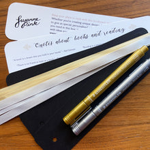 Load image into Gallery viewer, Bookmark making set resources with blank black bookmarks and gold and silver pens on a wooden background.
