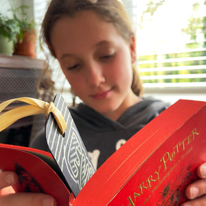 Girl reading a Harry Potter book with a bookmark inside, with a gold ribbon.