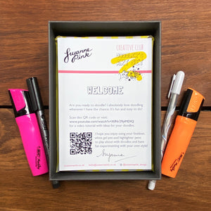 Doodler's Art Set with orange and pink highlighters, white gel pen and fineliner nestled in yellow recycled shredded paper.