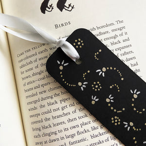 Black bookmark with a gold and silver dotted design and a silver ribbon on an open book.