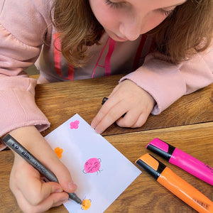 Child using fineliner to add details to orange and pink highlighter doodles.