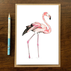 Flamingo greetings card with kraft envelope on wooden background with pencil.