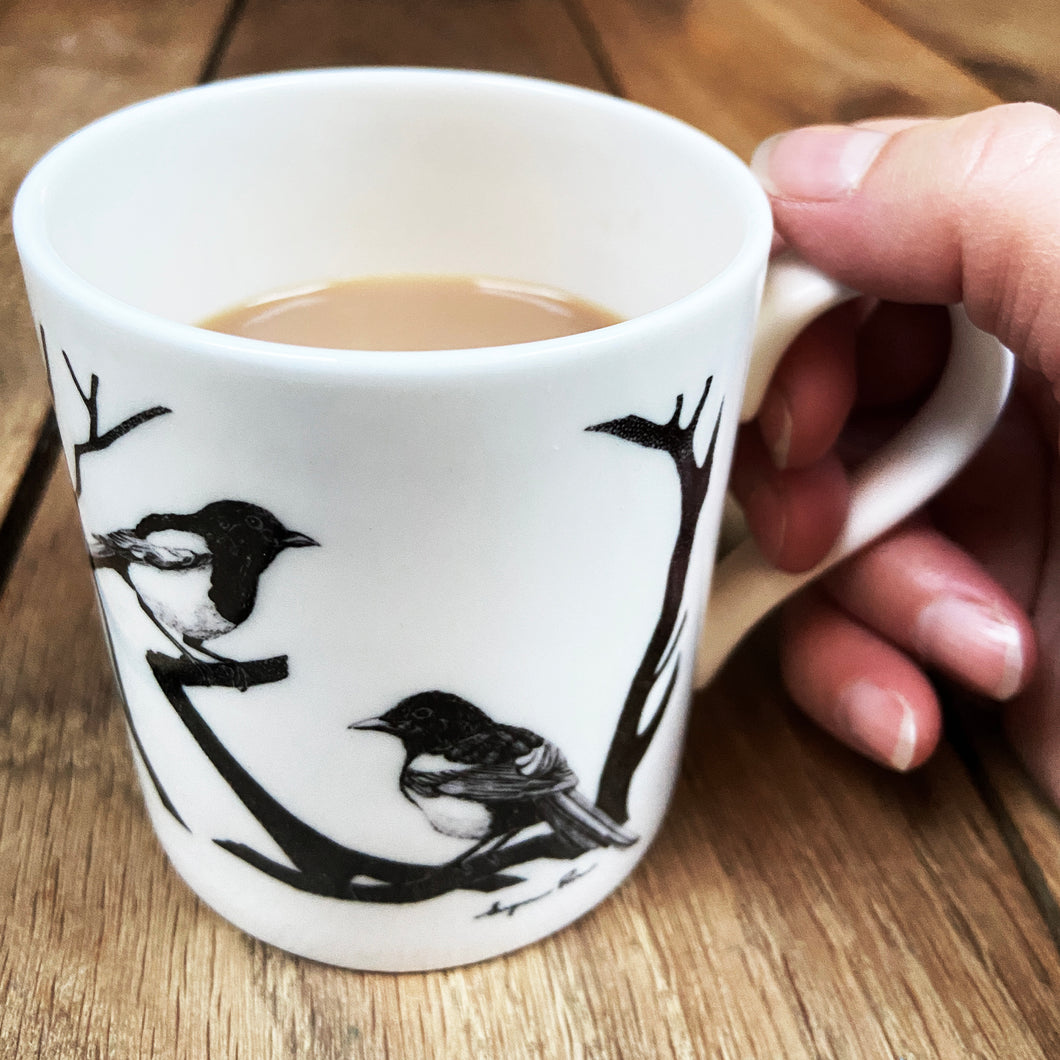 White fine bone china mug with two magpies design being held on a wooden background