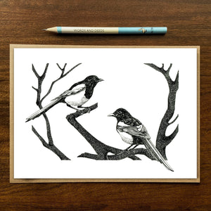 magpies greetings card on wood background with recycled kraft envelope and pencil.