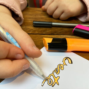 Child using fineliner to add details to orange and pink highlighter doodles.